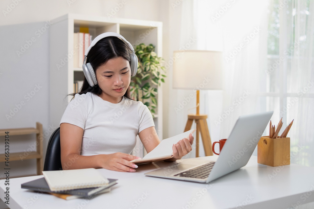 Young woman concentrating on reading notes while using laptop Young woman concentrating on reading notes while using laptop