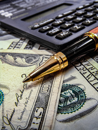 US Dollar money notes, pen and calculator on the table with narrow focus