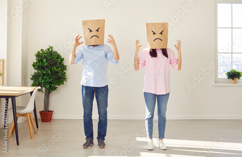 Couple with brown paper bags on their heads with angry and upset facial expressions painted on them. Couple raises hands due to mutual feelings of dissatisfaction and unspoken conflict in relationship