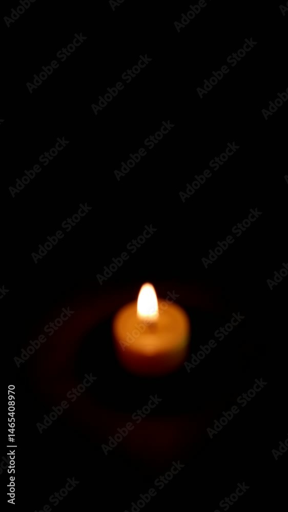 Una toma de cerca de una vela amarilla con llama desenfocada rodeada de varias luces con bombillos de varios colores en movimiento en la oscuridad. Video Vertical