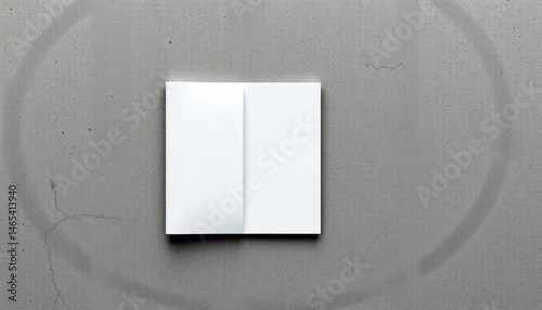 White folded invitation card on a grey grunge surface with circular shadow for mockups and presentations, minimalist style