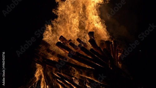 Towering flames engulf stacked logs in a dramatic fiery display. Slow motion