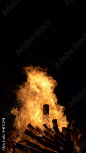 Dramatic fire engulfs wooden logs, with vivid orange and yellow hues. Vertical