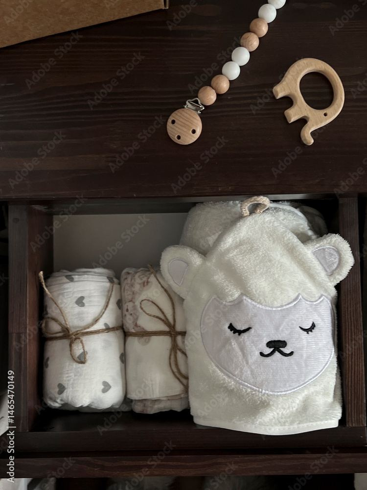 Muslin diapers, a white terry towel in the drawer of the bedside table. A wooden elephant teether, beads for a pacifier are on the bedside table. Children's minimalistic accessories for a newborn