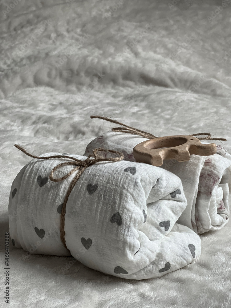 Two twisted muslin diapers and an elephant teether are lying on a milky-colored blanket. Children's fashion accessories