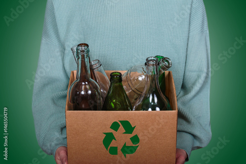 Cardboard box with glass bottles and green recycling symbol held by a person in eco-friendly clothing promoting responsible waste management and sustainability