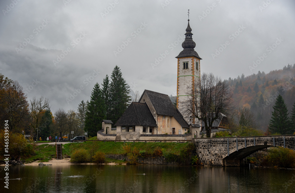 St. John the baptist's church rising from bohinj lake embankment on cloudy autumn day