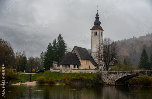Obraz na płótnie St. John the baptist's church rising from bohinj lake embankment on cloudy autumn day w salonie