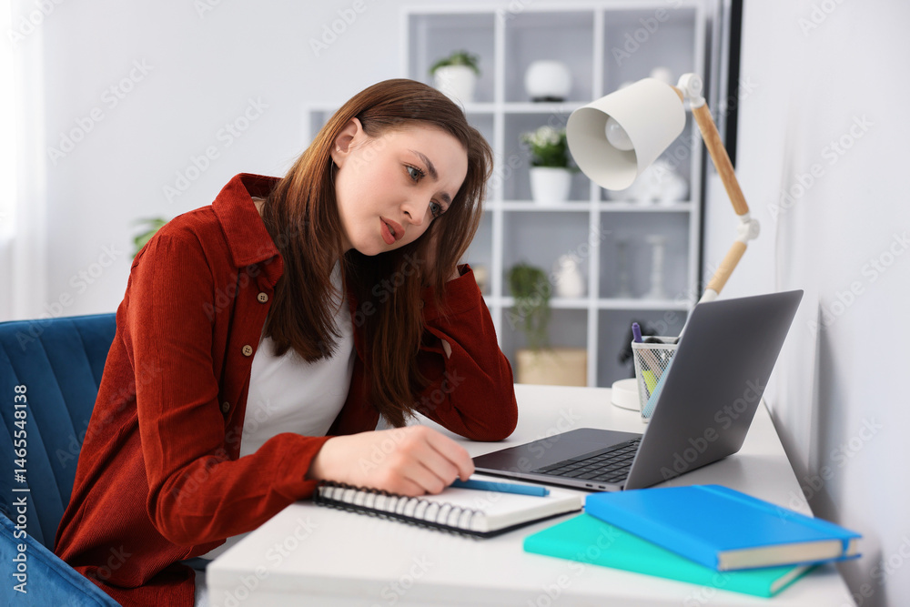 Teenage girl doing homework with laptop at table indoors Teenage girl doing homework with laptop at table indoors