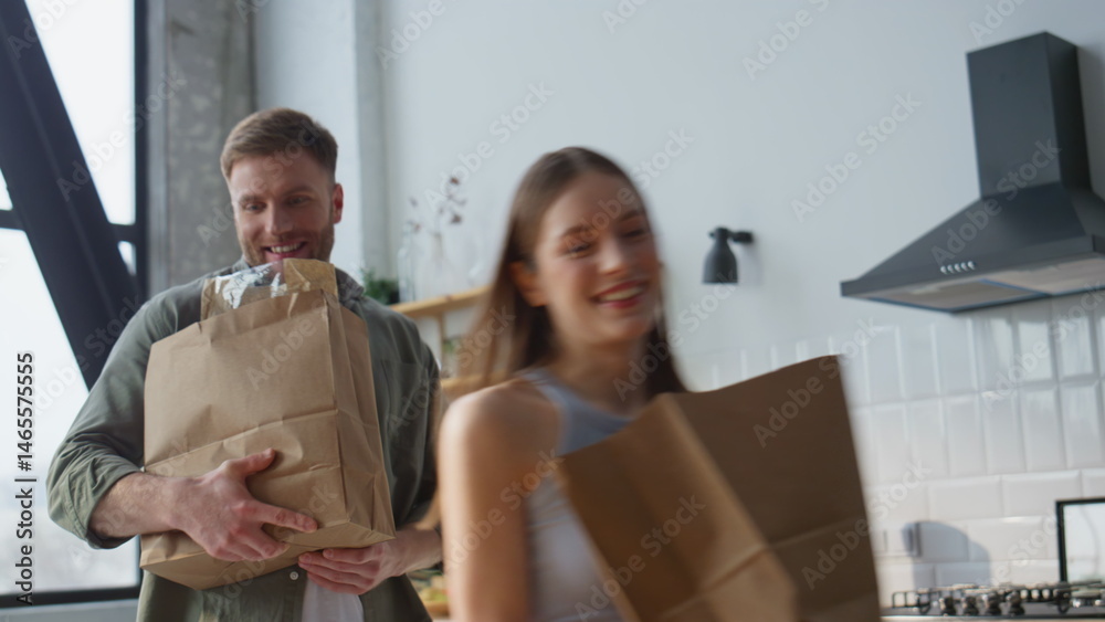 Cheerful couple carrying groceries in home kitchen. Two partners bringing food