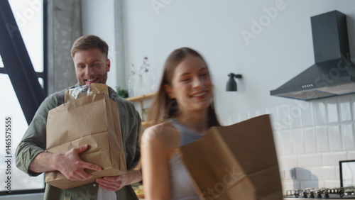 Obraz na płótnie Cheerful couple carrying groceries in home kitchen. Two partners bringing food w salonie