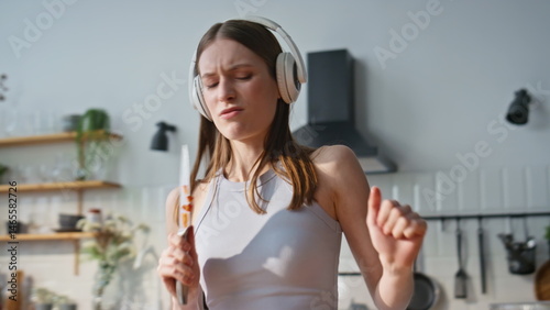 Singing woman chopping vegetables in headphones at domestic kitchen closeup. 