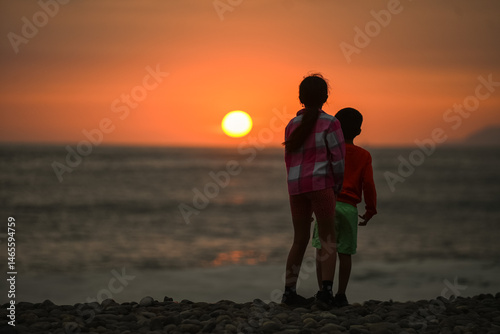 Sister and Little Brother Watching Sunset Over the Pacific Ocean at Lima Seashore, Peru