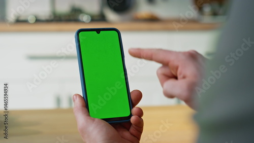 Hand pointing smartphone green screen browsing application in apartment closeup.