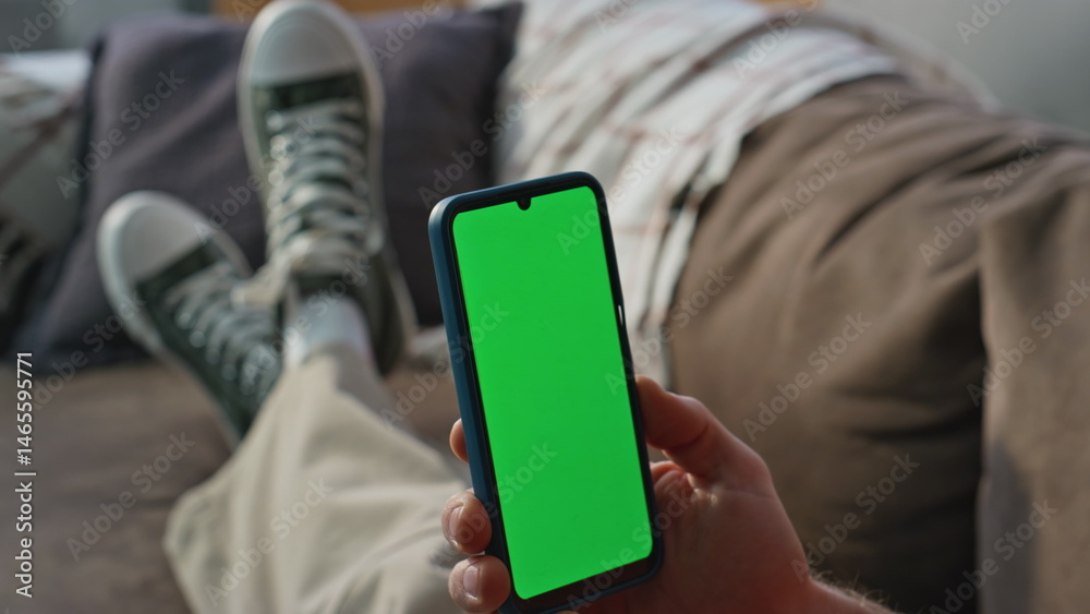 Man hand holding chromakey smartphone at home closeup. Guy watching green screen