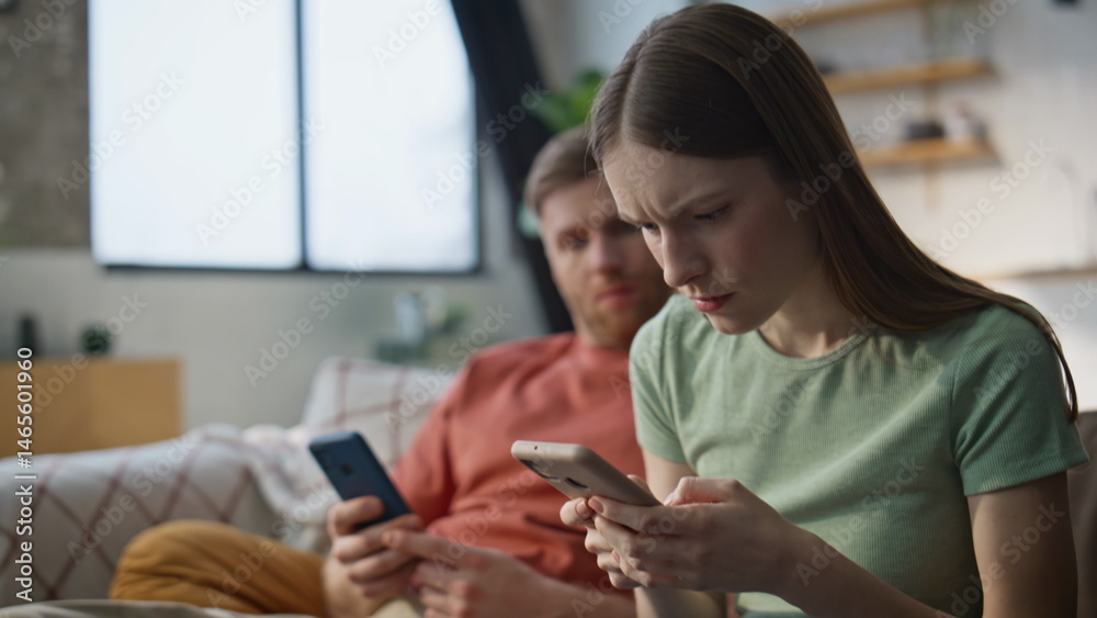 Worried wife showing message smartphone to husband sitting at couch closeup.