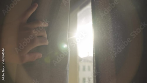 Hand pulls open window curtain to in dark room revealing sunlight shining in. Daylight from outside apartment or home shining bright creating lens flare. Hope and renewable energy or green solutions