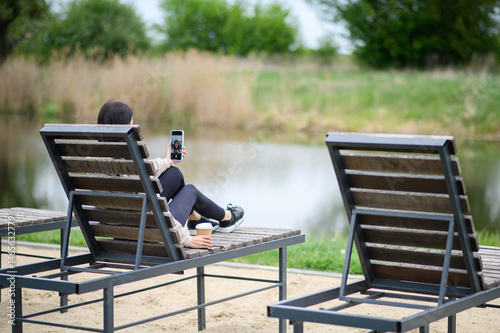 Woman making video call outdoors on lounge chair in park