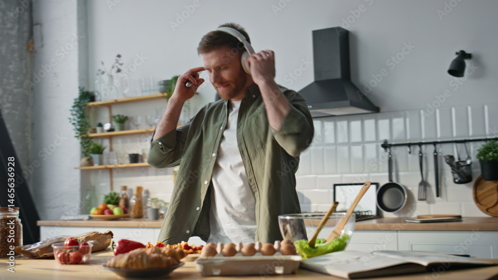 Smiling man chopping vegetables in kitchen dancing with headphones closeup.