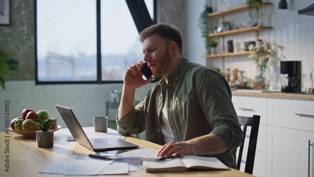 Thoughtful manager talking smartphone working on laptop at home office closeup