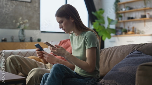 Serious couple looking cellphone sitting together at sofa living room closeup.