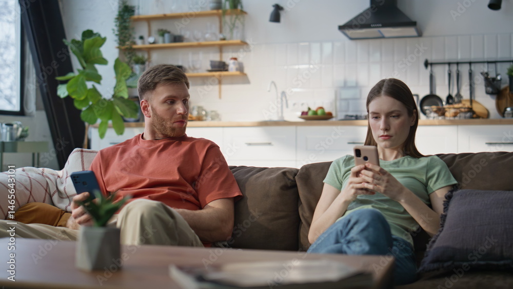 Offended pair using phones sitting together at couch. Serious man woman home