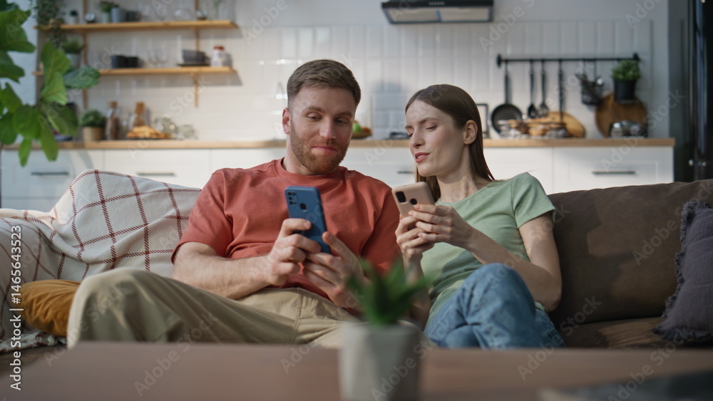 Cheerful couple relaxing sofa living room looking mobile phones. Laughing woman