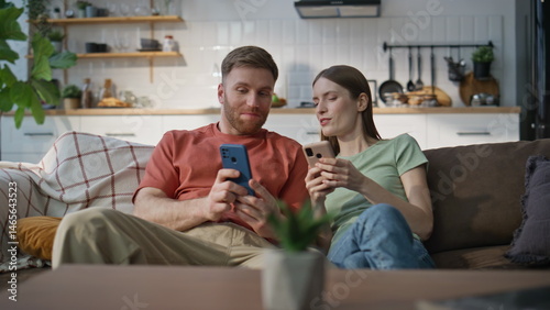 Obraz na płótnie Cheerful couple relaxing sofa living room looking mobile phones. Laughing woman w salonie