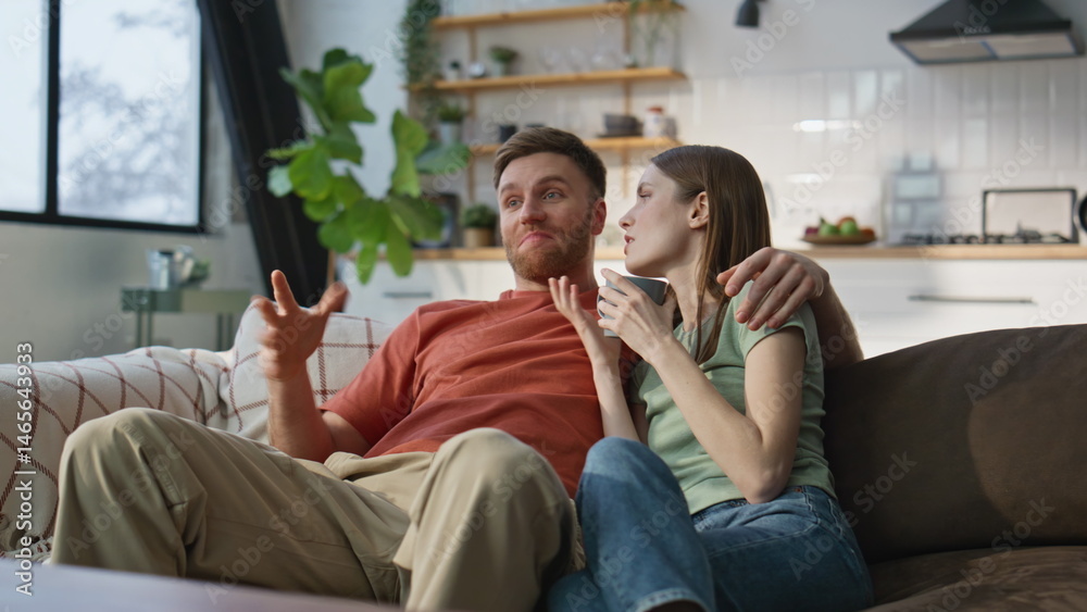 Relaxed spouses discussing movie sitting together at home sofa with coffee cup.