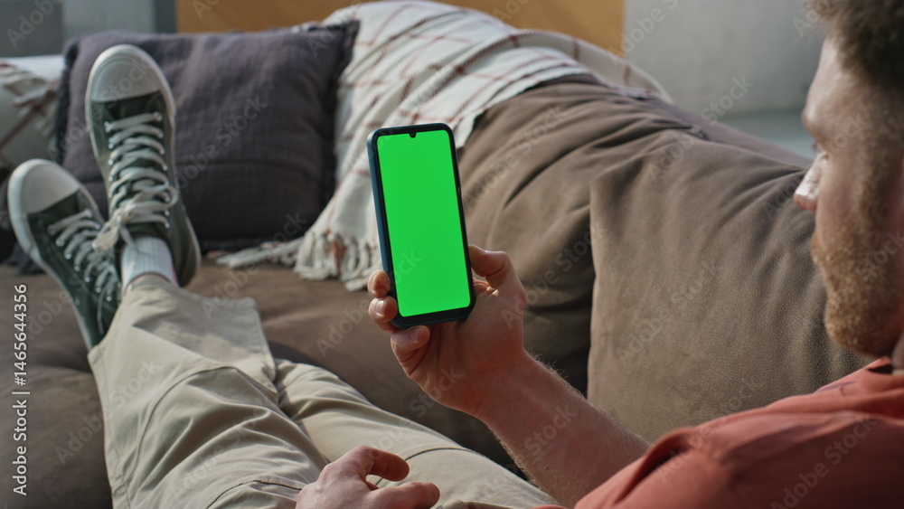 Guy browsing greenscreen cellphone relaxing on couch home closeup. Relaxed man