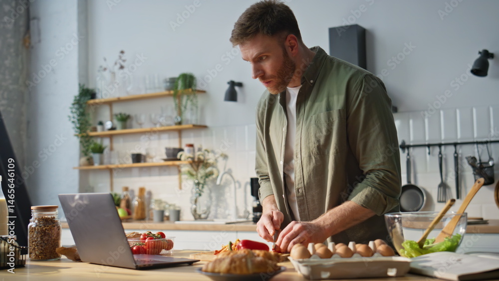 Guy watching video recipe chopping vegetables in kitchen. Guy slicing red pepper