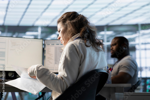 Woman overseeing server room, reading documentation paperwork, troubleshooting hardware. Supervisor doing inspection in server hub, reading technical files at computer desk