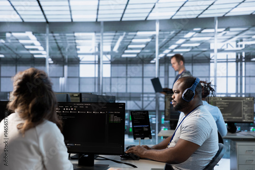 Obraz na płótnie African american man in data center coordinating deployment of server architecture, improving data processing speed. Worker listening music in server farm, configuring and testing equipment w salonie