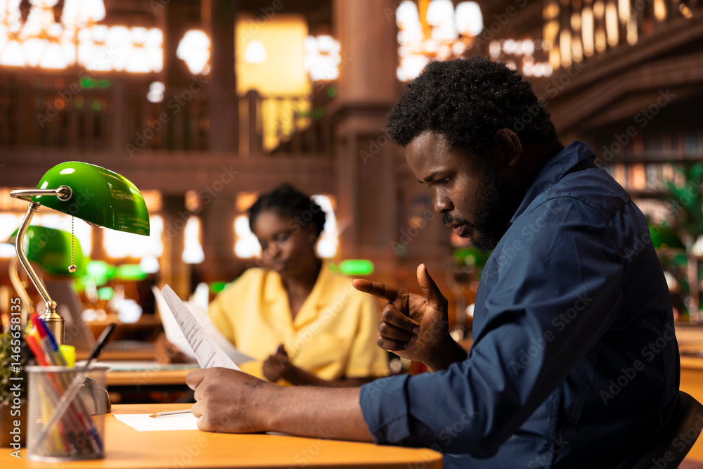 Ambitious university student researches academic topics in a library, using the campus study space to learn lessons and organize his course materials. Completing class notes for exams.