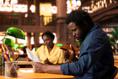 Obraz na płótnie Ambitious university student researches academic topics in a library, using the campus study space to learn lessons and organize his course materials. Completing class notes for exams. w salonie
