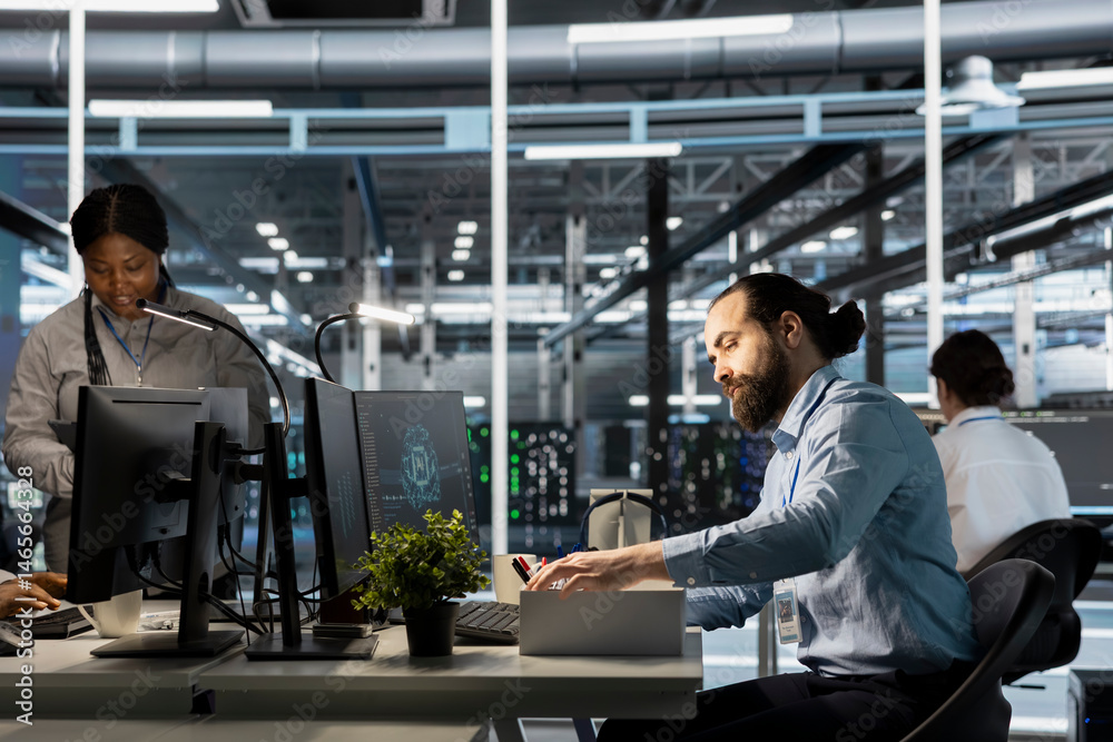 Upset engineer in data center packing personal items at workstation after being replaced by AI. Technician removing belongings from server hub workplace desk, fired by artificial intelligence