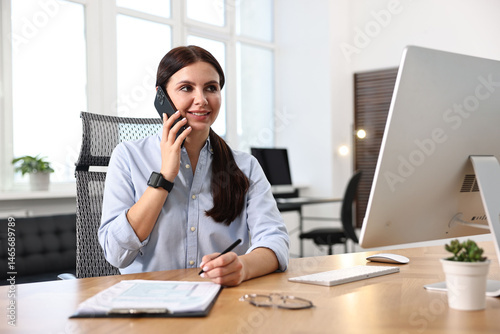 Woman talking on smartphone while working at table in office