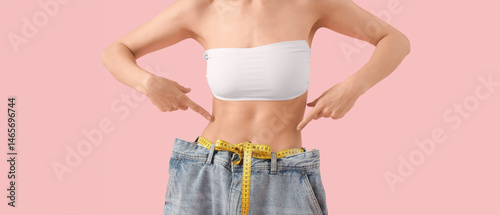 Billede på lærred Beautiful young woman with measuring tape wearing loose jeans on pink background, closeup
