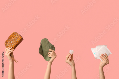 Female hands with reusable pad, menstrual cup and cosmetic bag on pink background