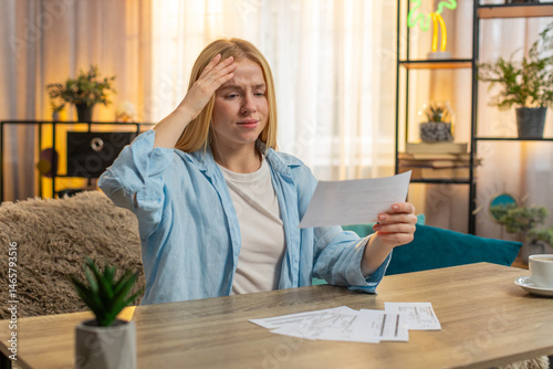 Young woman checks statement at home, eyes widening with alarm over unexpected expense. Girl sits at table sets paper aside, revealing tense realization of higher than normal cost of utility services