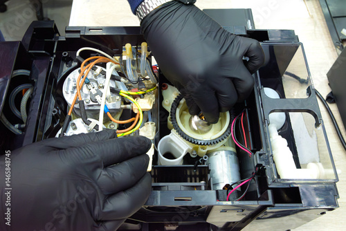 Schilderij op canvas Technician adjusting gear mechanism inside coffee machine during maintenance; visible wiring, motor, and internal heating system