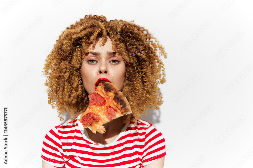 Young woman with curly hair enjoying a slice of pizza, expressing joy and indulgence, wearing a striped shirt, minimalist white background enhancing the vibrant colors