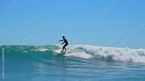 Person Surfing a Teal Ocean Wave Under a Clear Blue Sky With Water Spray and White Foam on Sunny Day