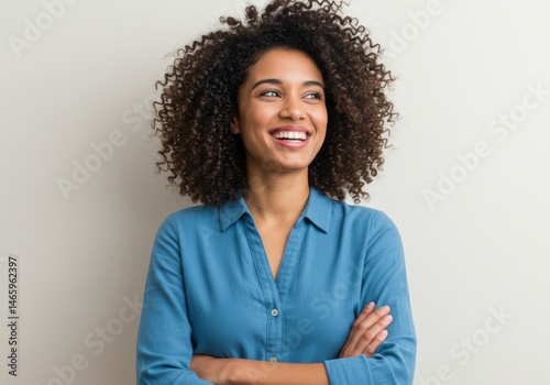 Woman with curly hair smiles wearing a blue shirt with arms folded isolated on white background