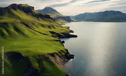 Stunning coastal landscape with rolling green fields, dramatic cliffs, sandy beaches, and sunlight breaking through clouds over the ocean horizon.