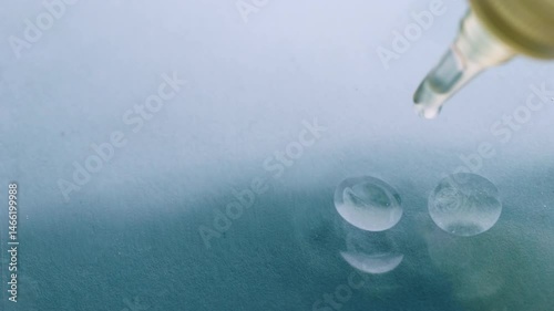 Close up view of glass pipette drop of oil on water surface background. Perfect for skincare, wellness, scientific themes etc., 