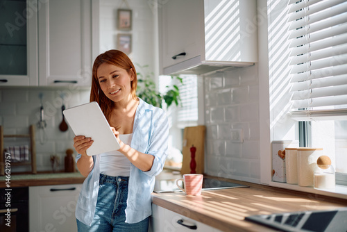 Happy woman surfing the net on touchpad in kitchen.