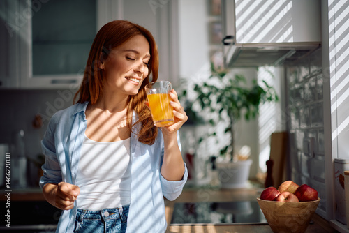 Foto Happy woman drinking orange juice in kitchen.