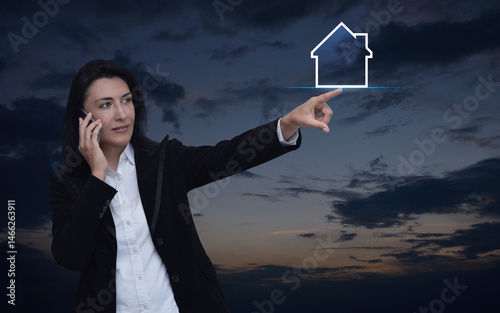 Businesswoman talking on her cell phone and pointing finger to house icon with copy space over sunset sky, Business real estate online concept