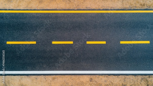 Aerial view of a freshly paved asphalt road with yellow lane markings and surrounding dirt.